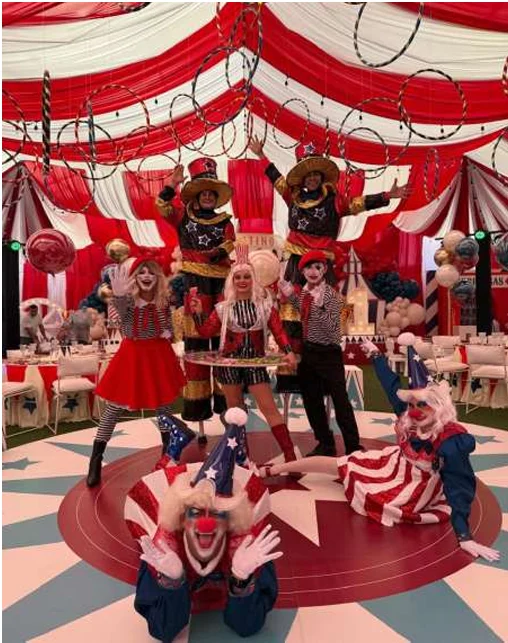 Payasos y artistas de circo posando en una carpa roja y blanca